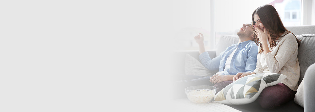 Couple laughing while sitting on a couch with popcorn.