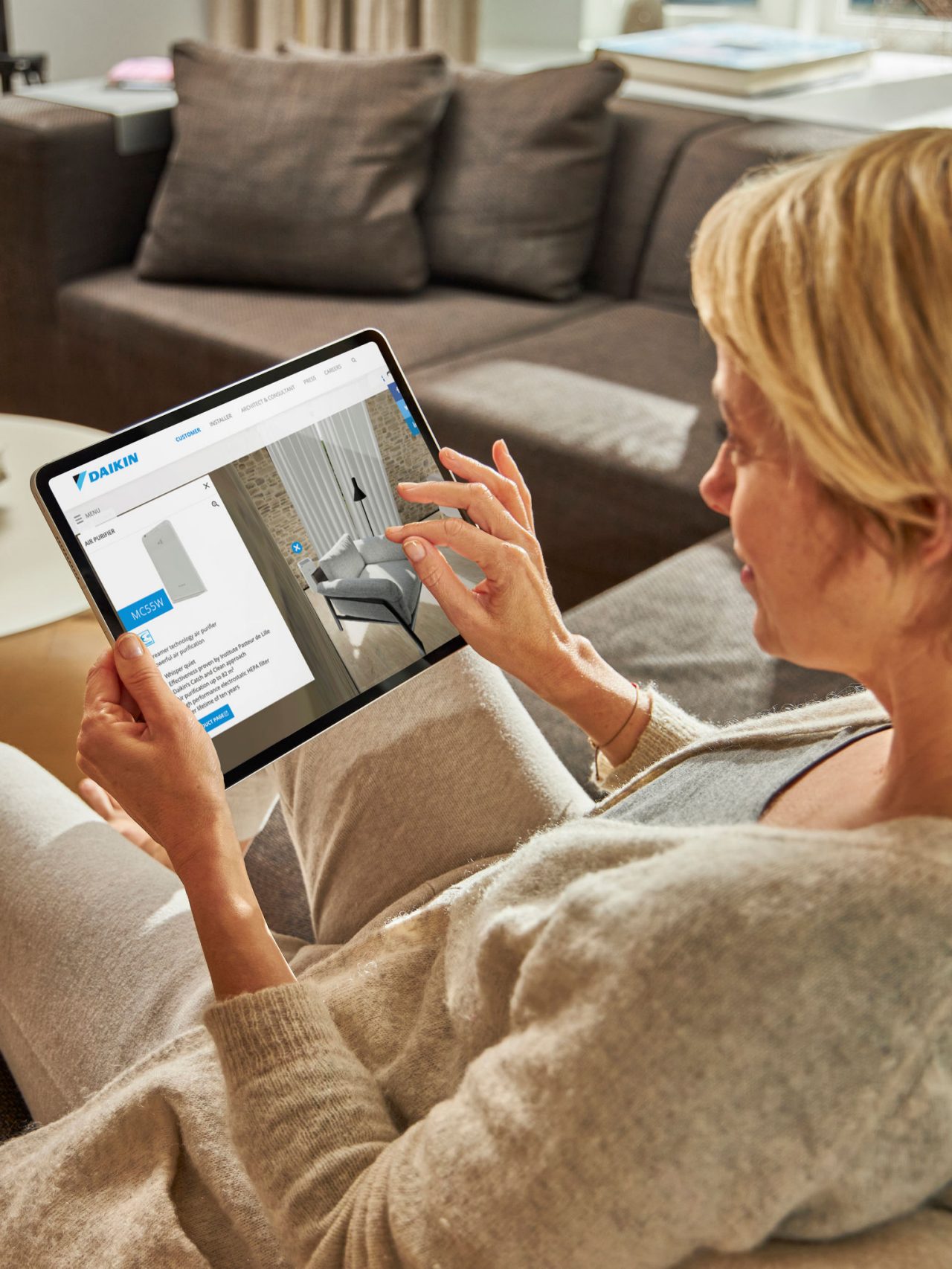 Woman sitting on a sofa viewing air conditioners on the virtual experience centre on his tablet